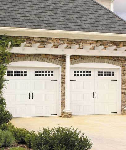 A home with two white carriage-style garage doors under a stone arch